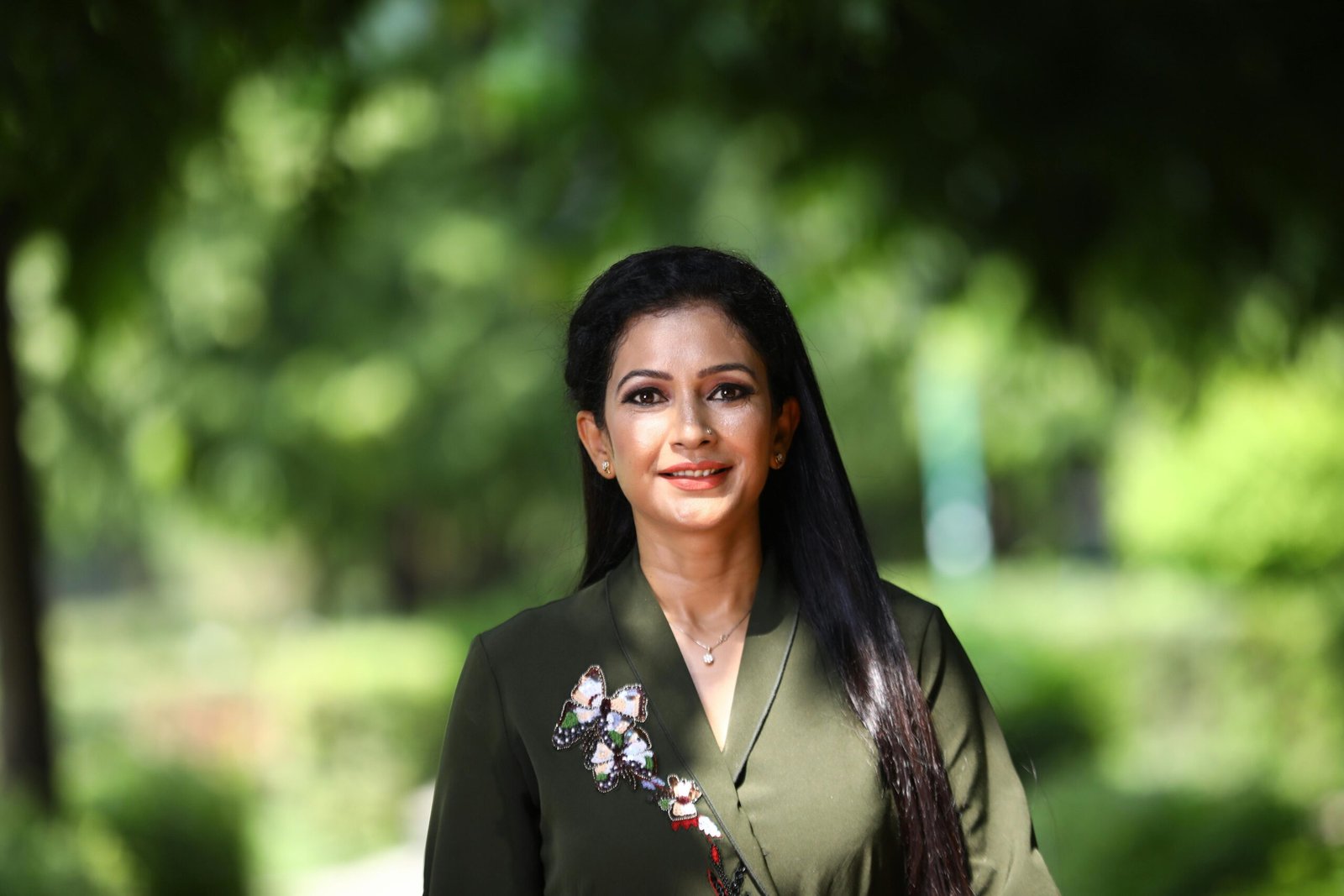 A smiling woman with long black hair wearing a green shirt outdoors, capturing elegance and fashion.