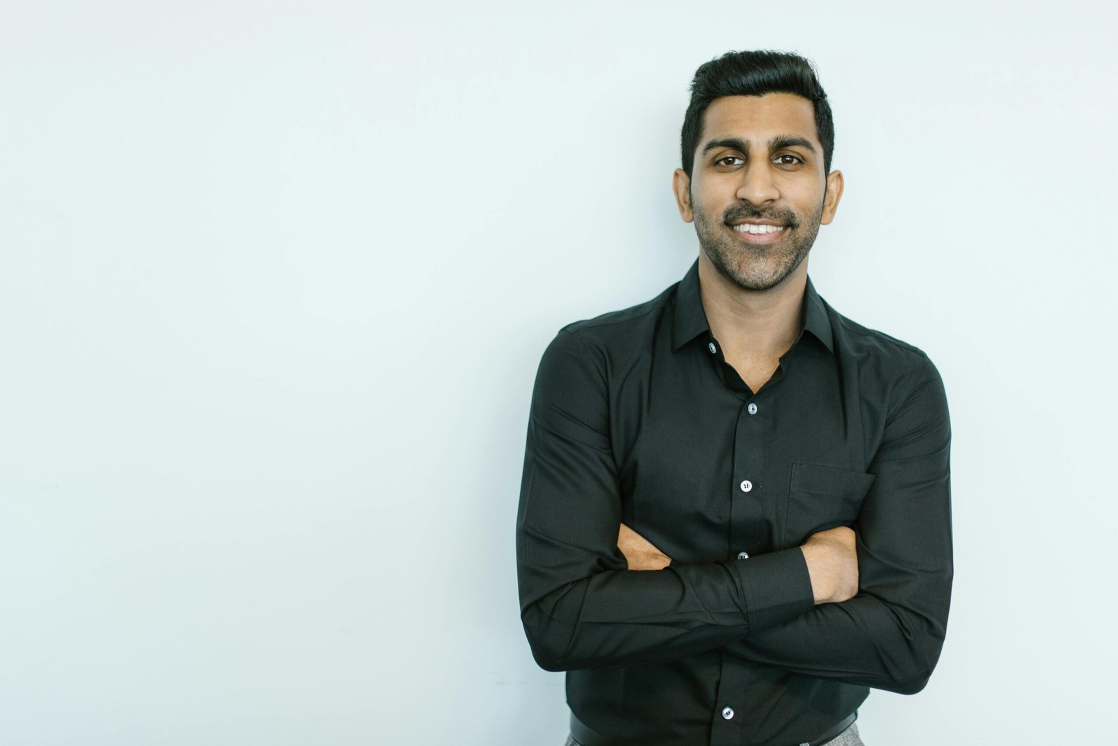 Portrait of a confident man in black shirt smiling against a plain background.
